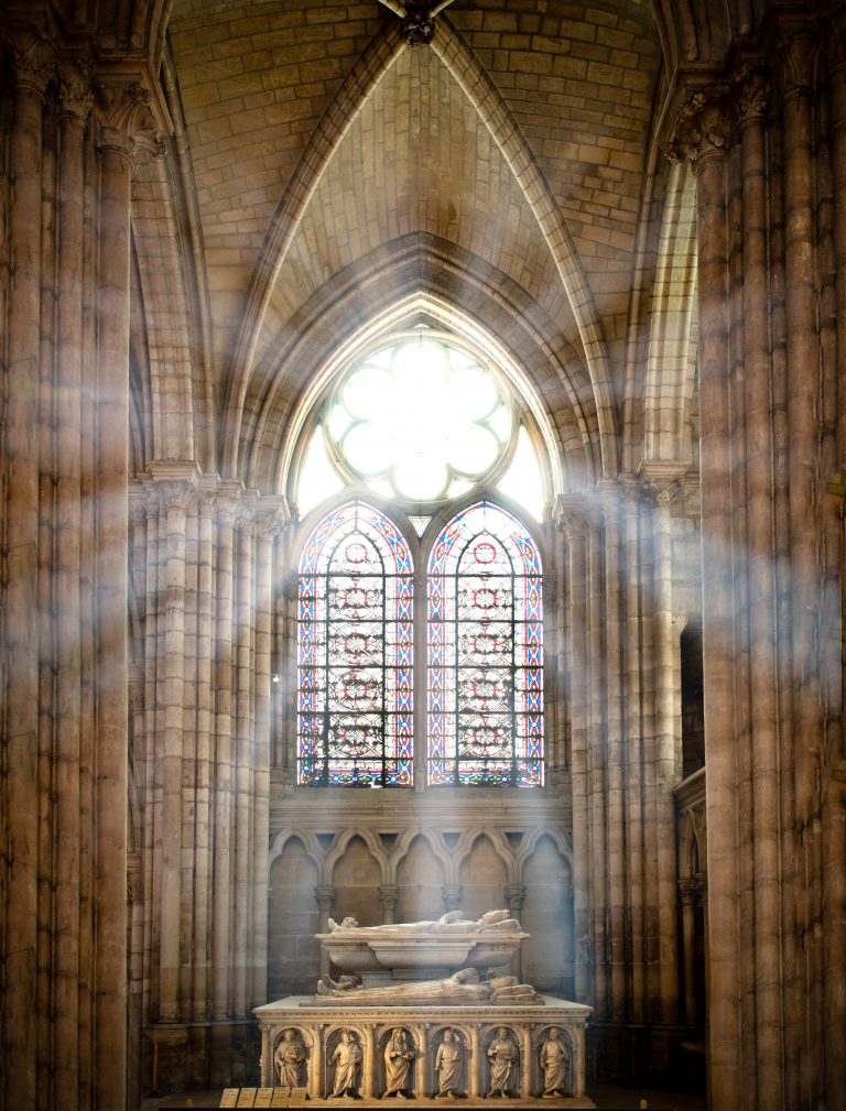 sun rays beaming through the old stained glass window of saint denis cathedral and lighting interior with tomb. Paris, France, Europe.