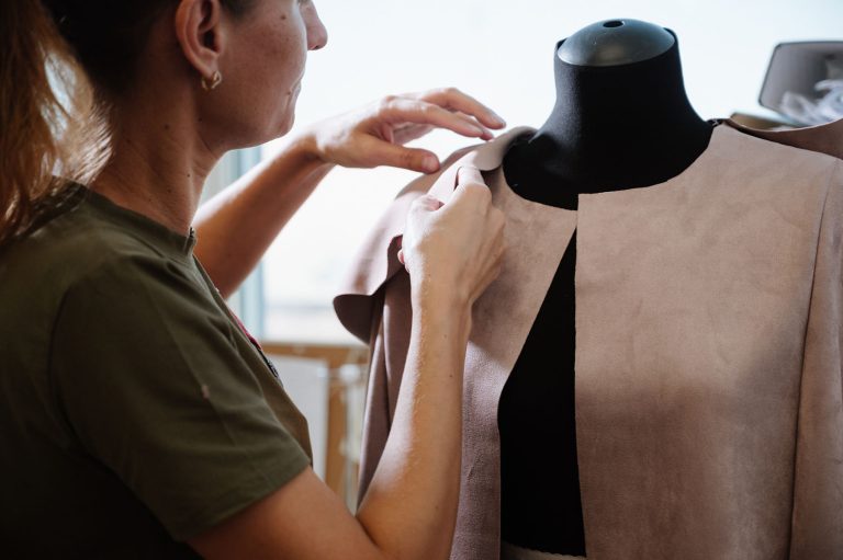 seamstress standing near mannequin and hanging up cloth in sewing studio.Creation or modelling of fashion clothes. Designer clothes concept